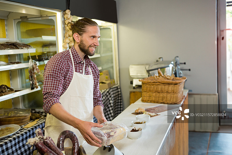 穿围裙的男肉店助手在熟食柜台上称重包装好的肉类，留有空白空间图片素材