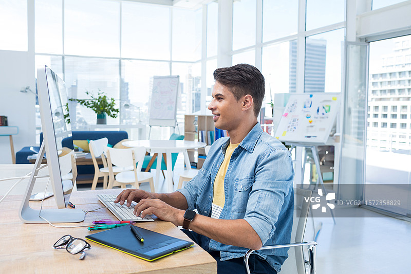 中年男子穿着牛仔衬衫，在开放式办公室使用电脑和绘图板，留有空白空间图片素材