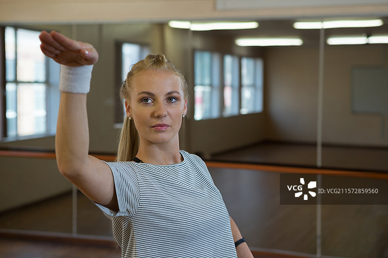 女性舞蹈学生在舞蹈室练习举臂姿势，佩戴着汗带，旁边有木制扶杆。图片素材