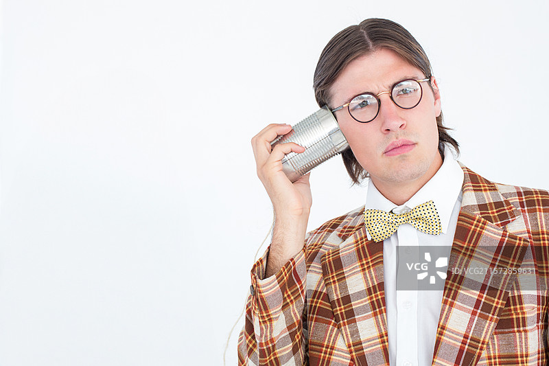 穿着格子西装和蝴蝶结的男人在白色背景前拿着罐头电话，留有空白空间图片素材