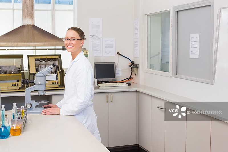 穿着实验室外套和眼镜的女性科学家，在实验室中使用显微镜和试管进行工作图片素材