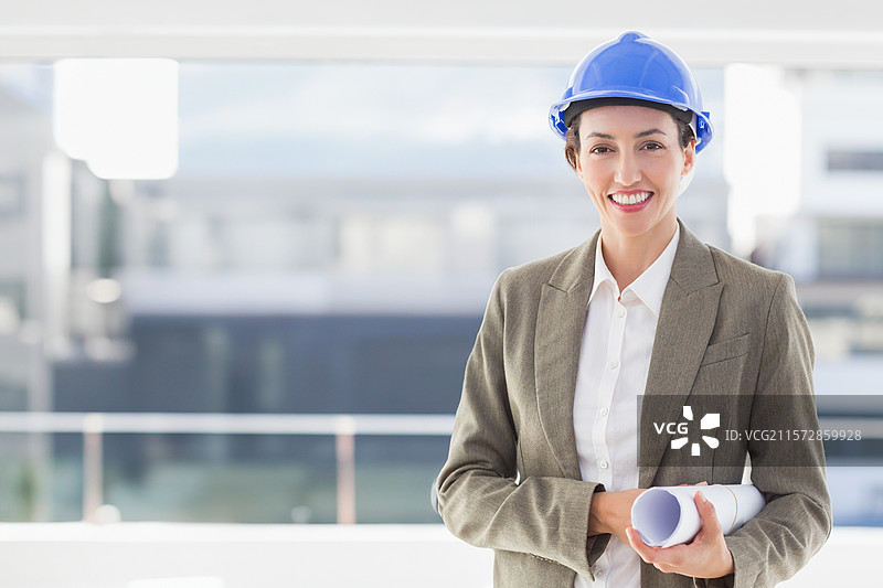 穿着西装的女性在阳台上戴着蓝色安全帽，手持计划，旁边有玻璃栏杆，留有空白空间图片素材