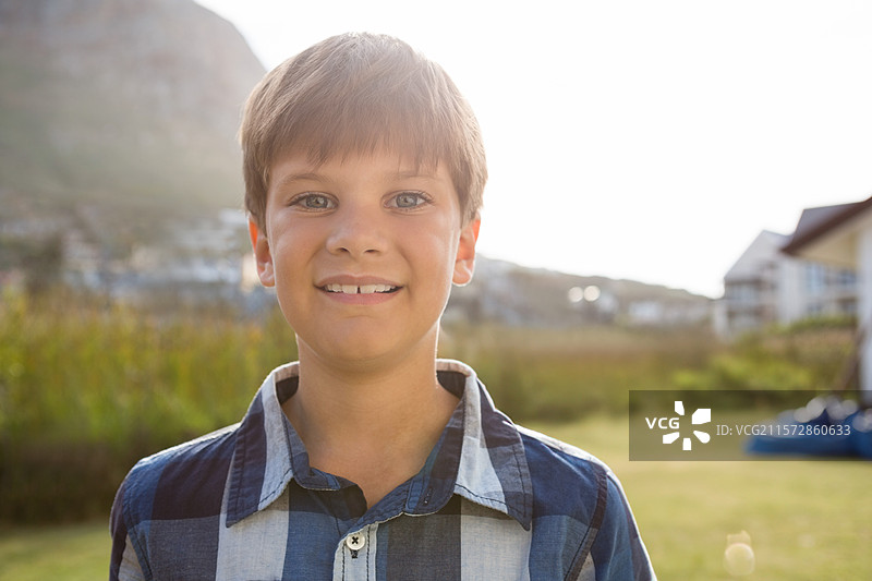 穿着蓝白格子衬衫的少年在阳光明媚的郊区草地上站着图片素材