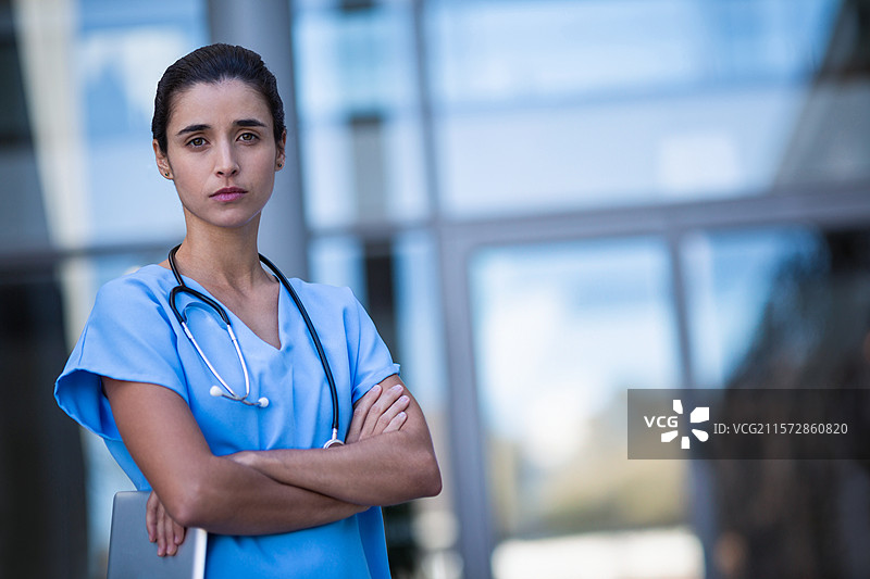 穿着护士服的女性护士站在医院外，手持平板电脑和听诊器，留有空白空间图片素材