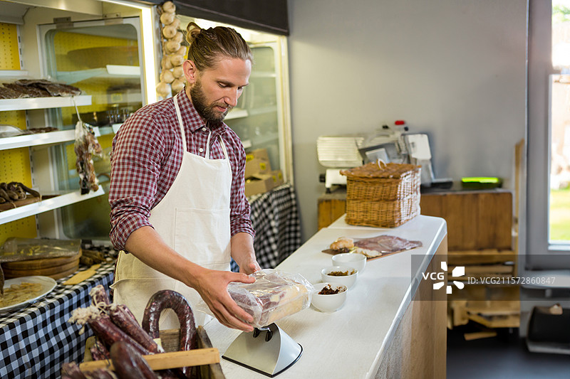 男肉贩在柜台后处理并称量真空包装的肉类产品，使用电子秤。图片素材