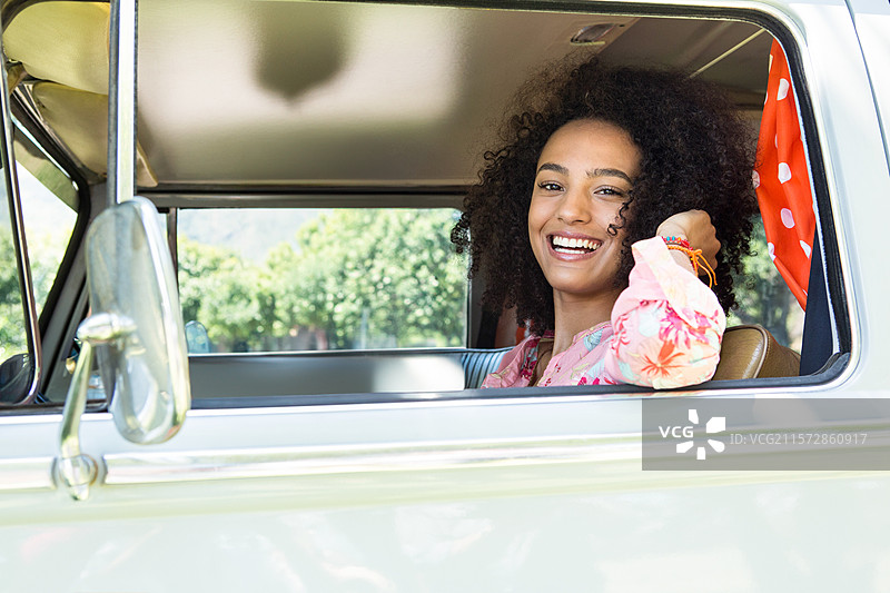 一位非裔美国女性坐在汽车的敞开窗户旁，穿着粉色衬衫，佩戴手链，留有空白空间。图片素材