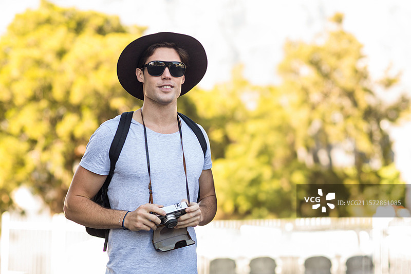 男性摄影师在阳光明媚的花园中戴着宽边帽，手持测距相机，留有空白空间图片素材