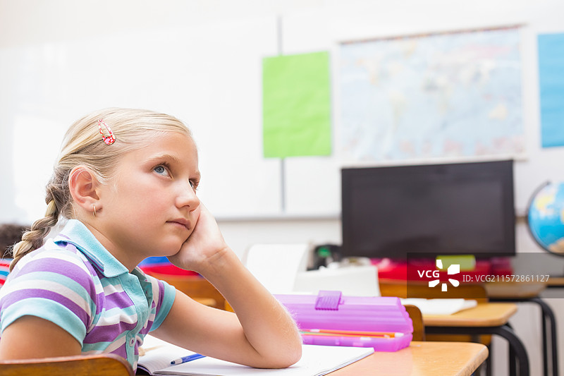 女学生坐在学校的桌子前，用铅笔盒里的文具在笔记本上写字，留有空白空间。图片素材