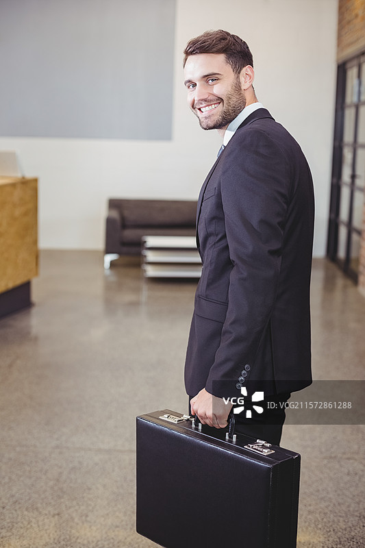 黑色皮革公文包放在办公室大堂的抛光混凝土地板上，旁边有一张白色咖啡桌。图片素材