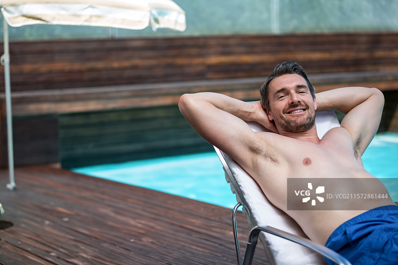 白色休闲椅静静地放在深色木质泳池甲板上，旁边有一把大遮阳伞，背景是山景。图片素材