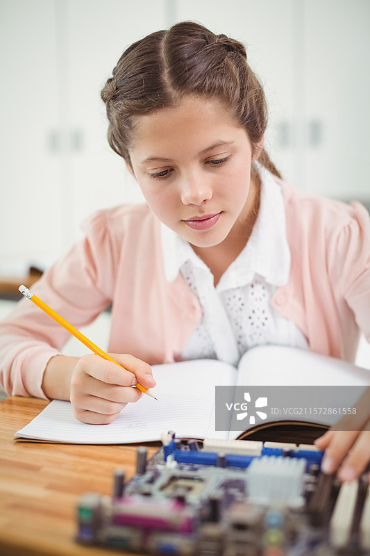 女学生在实验室的木桌上写开放笔记本，检查电路板。图片素材