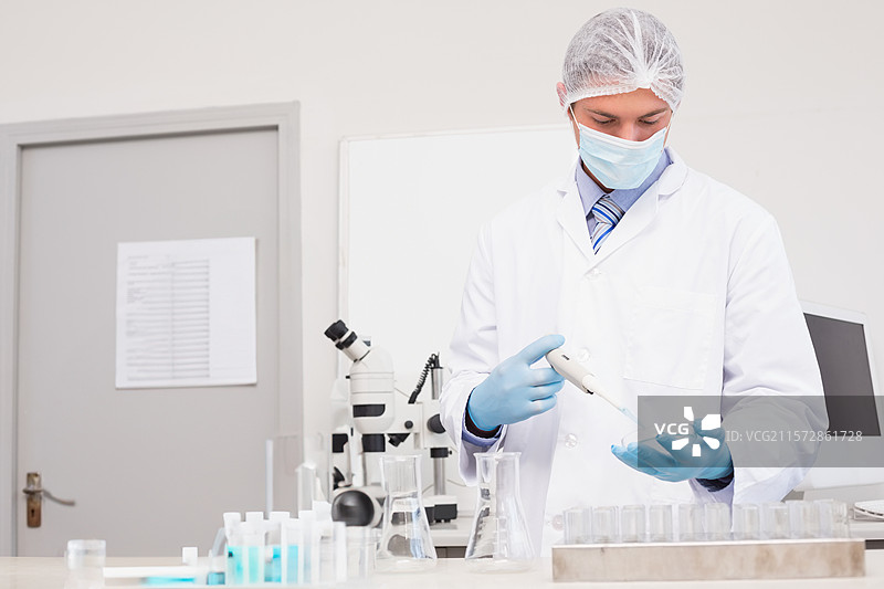 可调式移液器将蓝色液体分配到实验室工作台上的试管架中，周围有玻璃器皿。图片素材