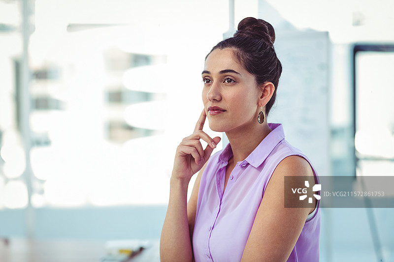 穿着淡紫色上衣的女性用右手托着下巴，凝视着白板旁的桌子，留有空白空间。图片素材