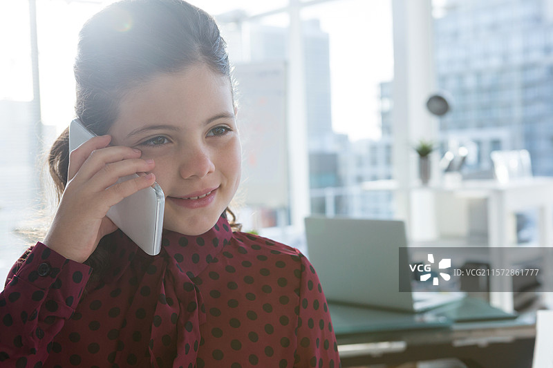 穿着波点衬衫的孩子在办公桌旁的窗户前拿着智能手机，旁边有笔记本电脑，留白空间。图片素材
