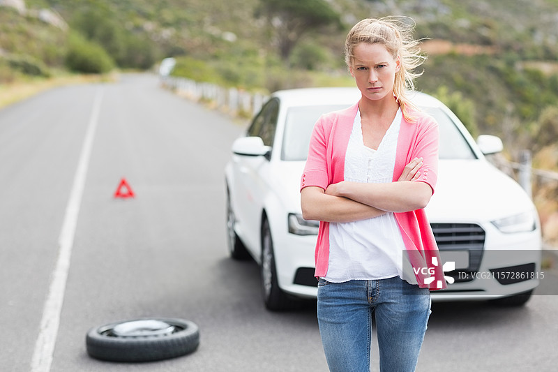 女性司机在白色轿车旁的坡道上更换备胎，旁边有警告三角架，留有空白空间。图片素材