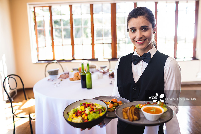 女服务员在宴会厅中端着装满沙拉、汤、面包和开胃菜的托盘，留有空白空间。图片素材