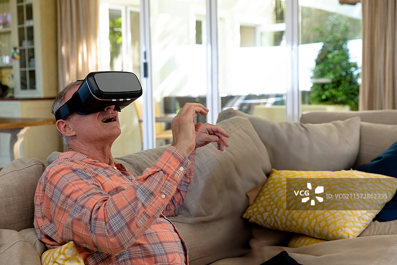 虚拟现实头盔放在米色沙发上，旁边是滑动门，展示着户外的绿色植物。图片素材