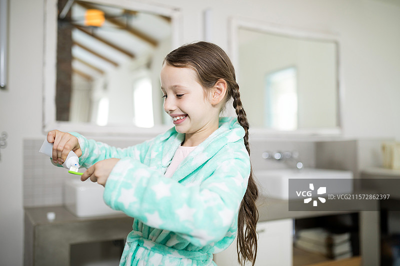 小女孩穿着星星浴袍，在浴室台面上挤牙膏到牙刷上，留有空白空间图片素材