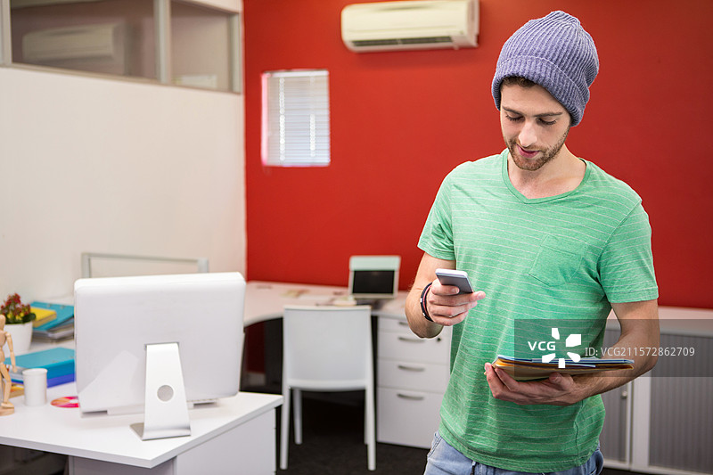 男子在红色墙壁的办公室里查看手机信息，旁边有平板显示器，留有空白空间。图片素材
