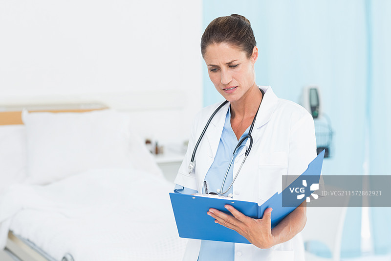 医院病床上铺着洁白的床单，旁边有生命体征监测仪和蓝色的夹板放在桌子上。图片素材