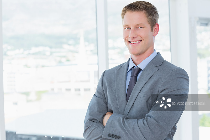 企业高管双臂交叉站在落地窗前，窗外是城市天际线。图片素材