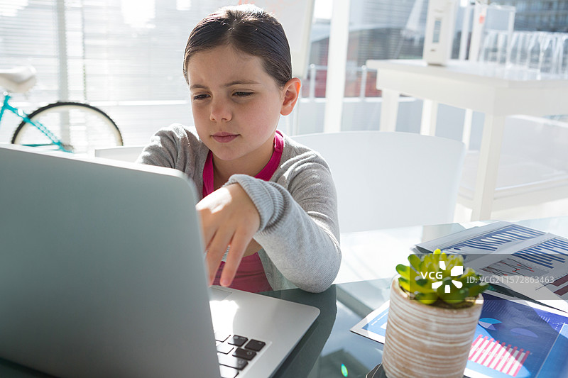 女孩在家中的办公室用笔记本电脑学习，旁边有多肉植物和图表，旁边还有一个自行车轮。图片素材