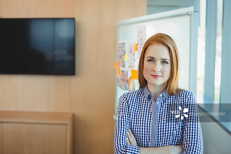 穿着格子衬衫的女性站在企业会议室里，正在查看白板上的笔记。图片素材