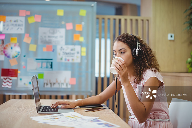 身穿粉色连衣裙和耳机的非裔美国女性在办公室使用笔记本电脑，留白空间图片素材