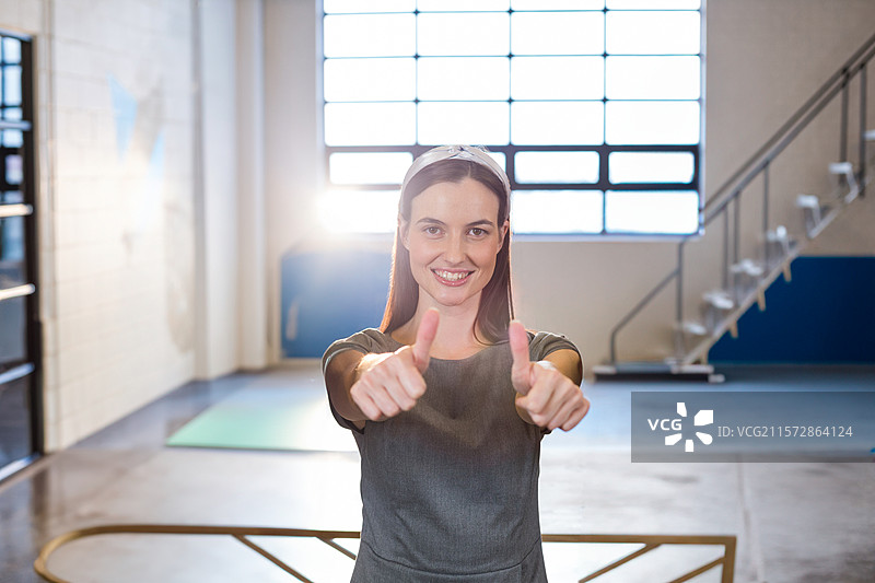 女性站在工作室中央，脚下是绿色瑜伽垫，旁边有芭蕾舞杆，窗户是格子图案。图片素材