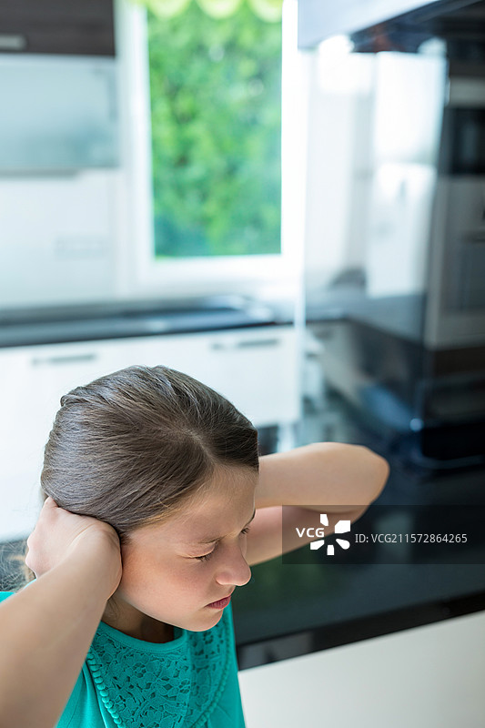 女孩在厨房台面上捂住耳朵，面露痛苦，旁边有咖啡机和白色橱柜。图片素材