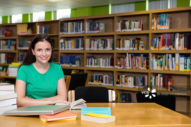 穿着绿色衬衫的女性在图书馆桌子上学习，面前有一本打开的书、笔记本和笔记本，留有空白空间。图片素材