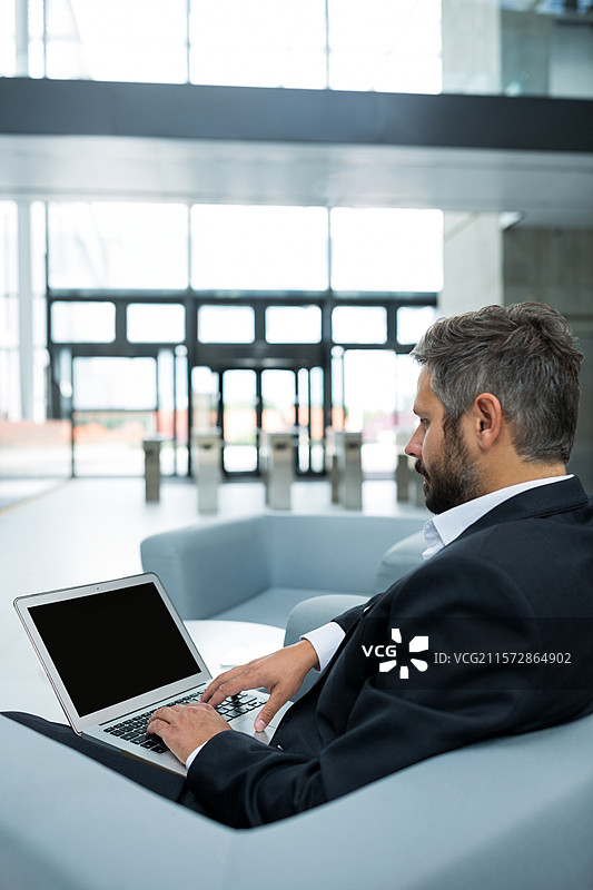 男人坐在扶手椅上，靠近玻璃门，正在笔记本电脑上打字，企业大堂的旋转门，留白空间图片素材