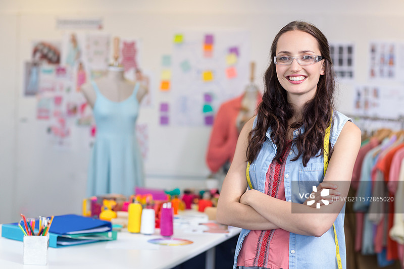 穿着测量带的女性在设计工作室中摆姿势，旁边有模特和线轴，留白空间图片素材