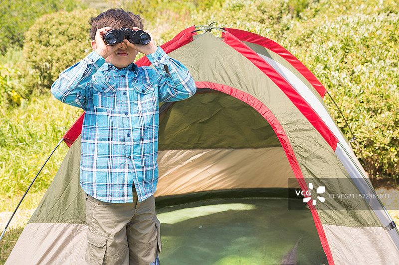 黑色双筒望远镜靠在橄榄绿色的圆顶帐篷上，周围是茂密的灌木丛，草地上。图片素材