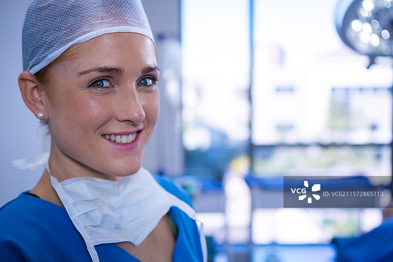 女性外科医生在手术室内，佩戴手术帽和口罩，站在手术灯下。图片素材