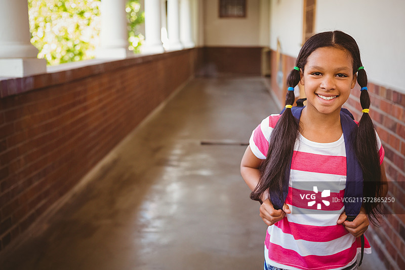 在学校走廊里站着的学生，背着深蓝色的背包，手里拿着发绳，留有空白空间。图片素材