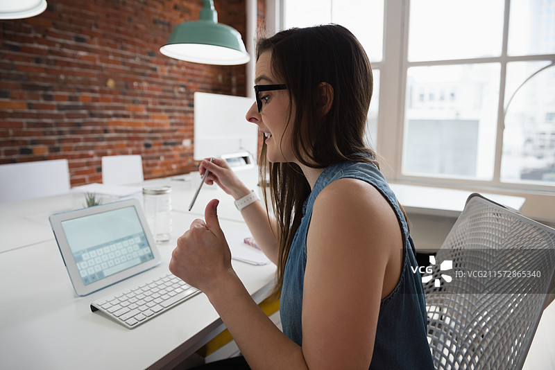 女性在现代办公室工作区举着手写笔并竖起大拇指图片素材