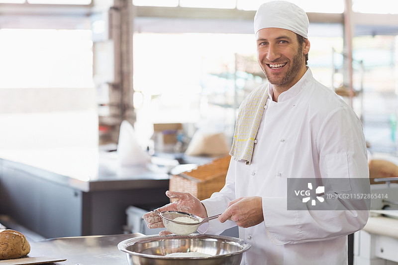 男厨师穿着厨师外套，正在面包店厨房用筛子将面粉筛入碗中，留有空白空间。图片素材