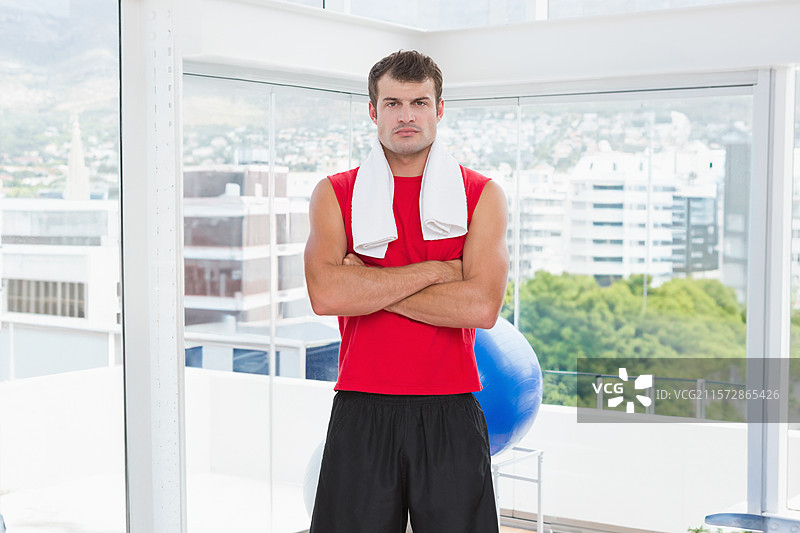 一位非裔美国男性站在健身工作室的大窗户旁，手里拿着毛巾和健身球。图片素材