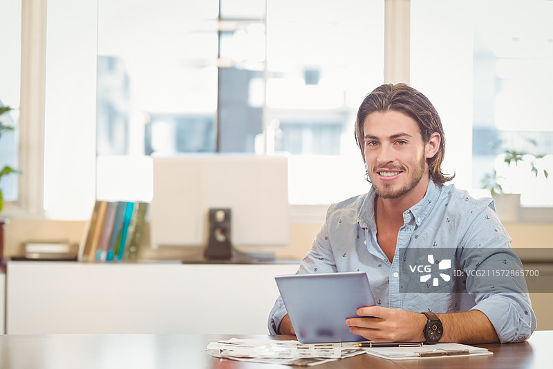 男性办公室工作人员手持平板电脑，在大窗户旁的木桌上查看打印照片图片素材