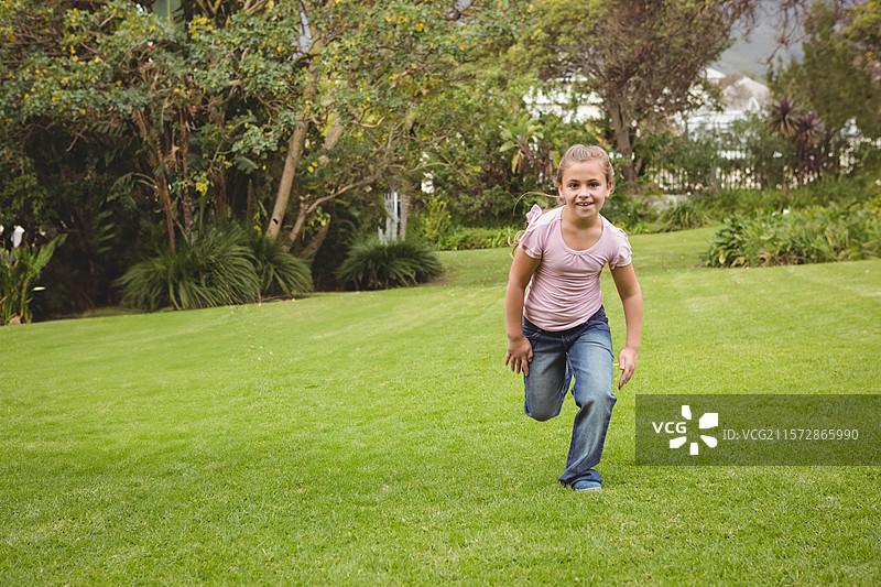 穿着粉色衬衫和蓝色牛仔裤的女孩在住宅后院的草坪上奔跑图片素材