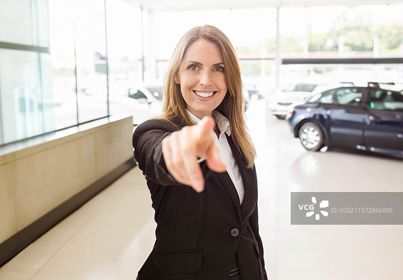 穿着商务服装的女性在展厅指着摄像机，身后是一辆深色SUV和一辆浅色轿车。图片素材