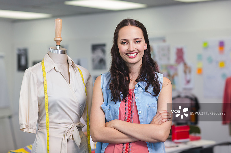 女性设计师站在时尚工作室，旁边是模特上的裹身裙，手里拿着黄色的卷尺。图片素材