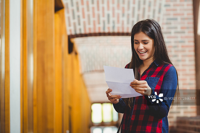 穿着格子衬衫的女性站在图书馆走廊，阅读折叠的信件，留有空白空间图片素材