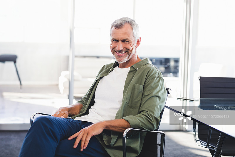 坐在会议桌上的微笑老年男子，手持笔记本和钢笔，旁边留有空白空间图片素材