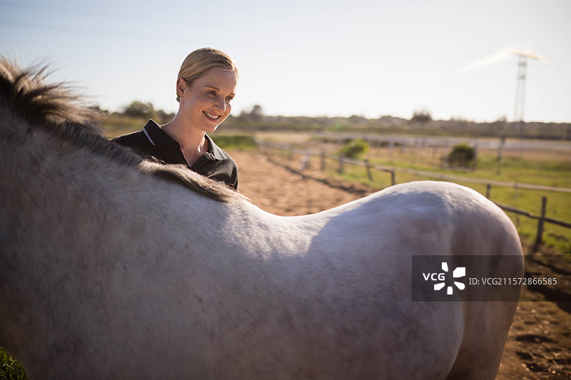 穿着 polo 衫的女性站在灰色马旁边，靠近围栏，马场上有电力塔，留有空白空间。图片素材