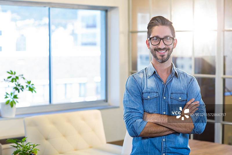 男子站在办公室休息区的浅色沙发和玻璃隔断旁，周围有盆栽植物，留有空白空间。图片素材