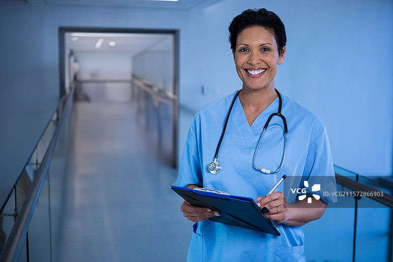 穿着护士服的女性护士在医院走廊里手持夹板和笔，脖子上挂着听诊器，留有空白空间。图片素材