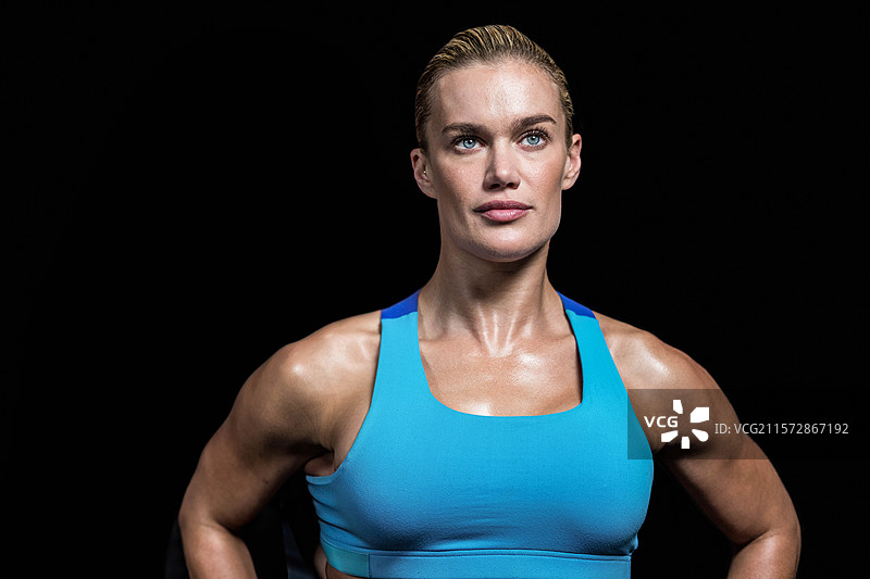 身材健美的女性自信地站在工作室里，穿着明亮的蓝色运动胸罩，背景为黑色。图片素材