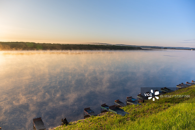 初夏清晨黑龙江呼玛县黑龙江畔，初升太阳照亮江面升腾的晨雾，散发金光，岸边一排钓鱼台图片素材